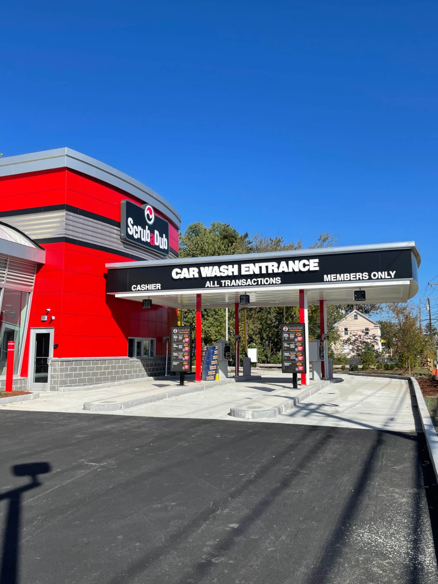 Bright red ScrubaDub building and a canopy reading Car Wash Entrance with pay stations under a clear blue sky