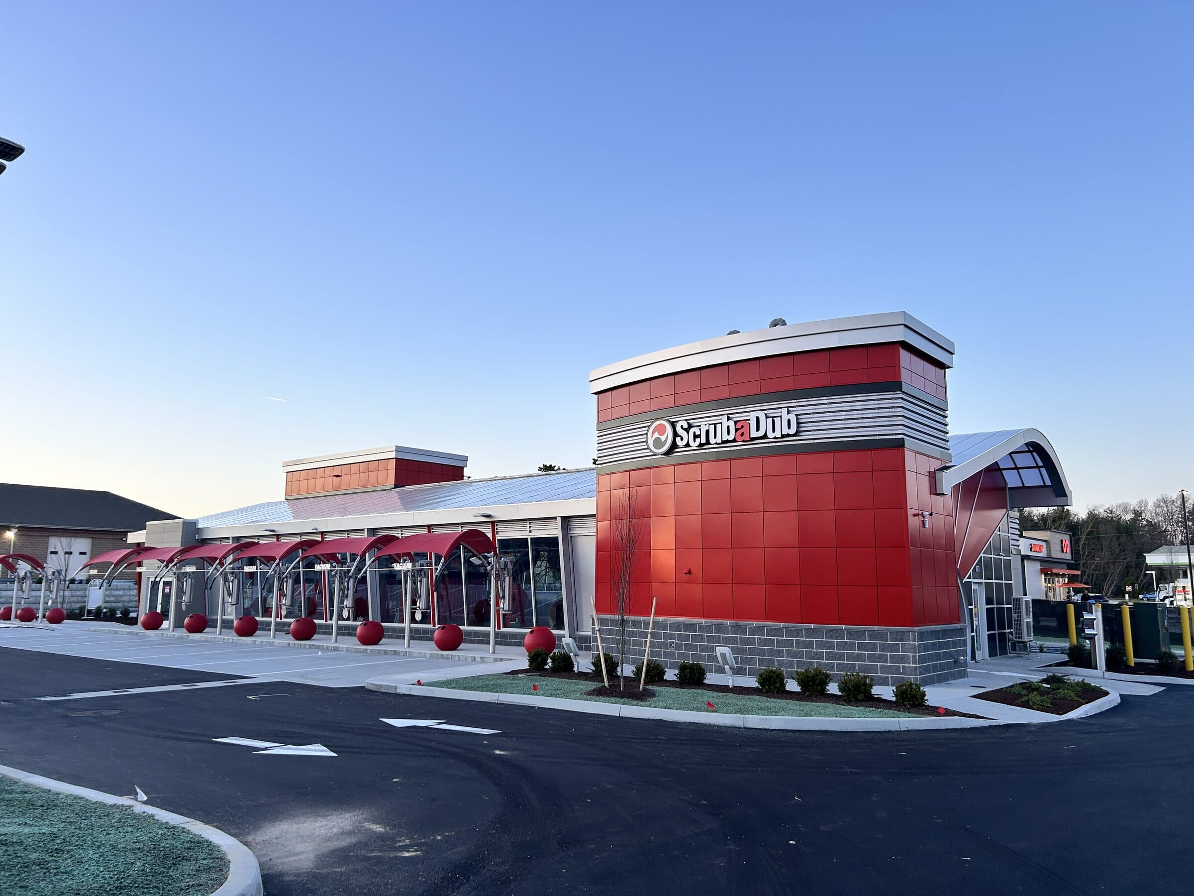 New red ScrubaDub car wash building with a row of red-canopied vacuum stations under a clear evening sky