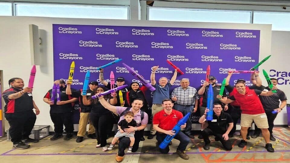 ScrubaDub team members holding giant inflatable crayons in front of a Cradles to Crayons backdrop