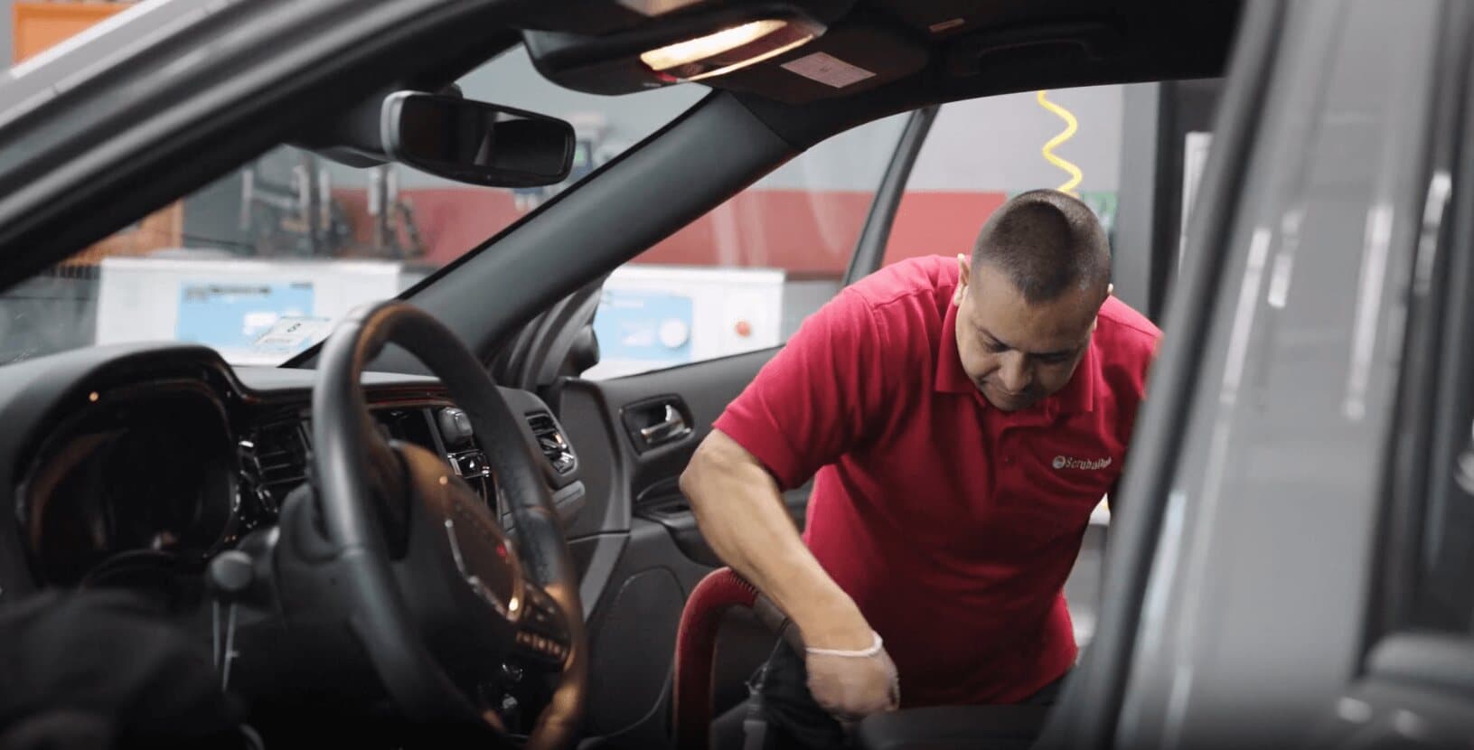 ScrubaDub attendant in a red polo vacuuming the front of a car interior