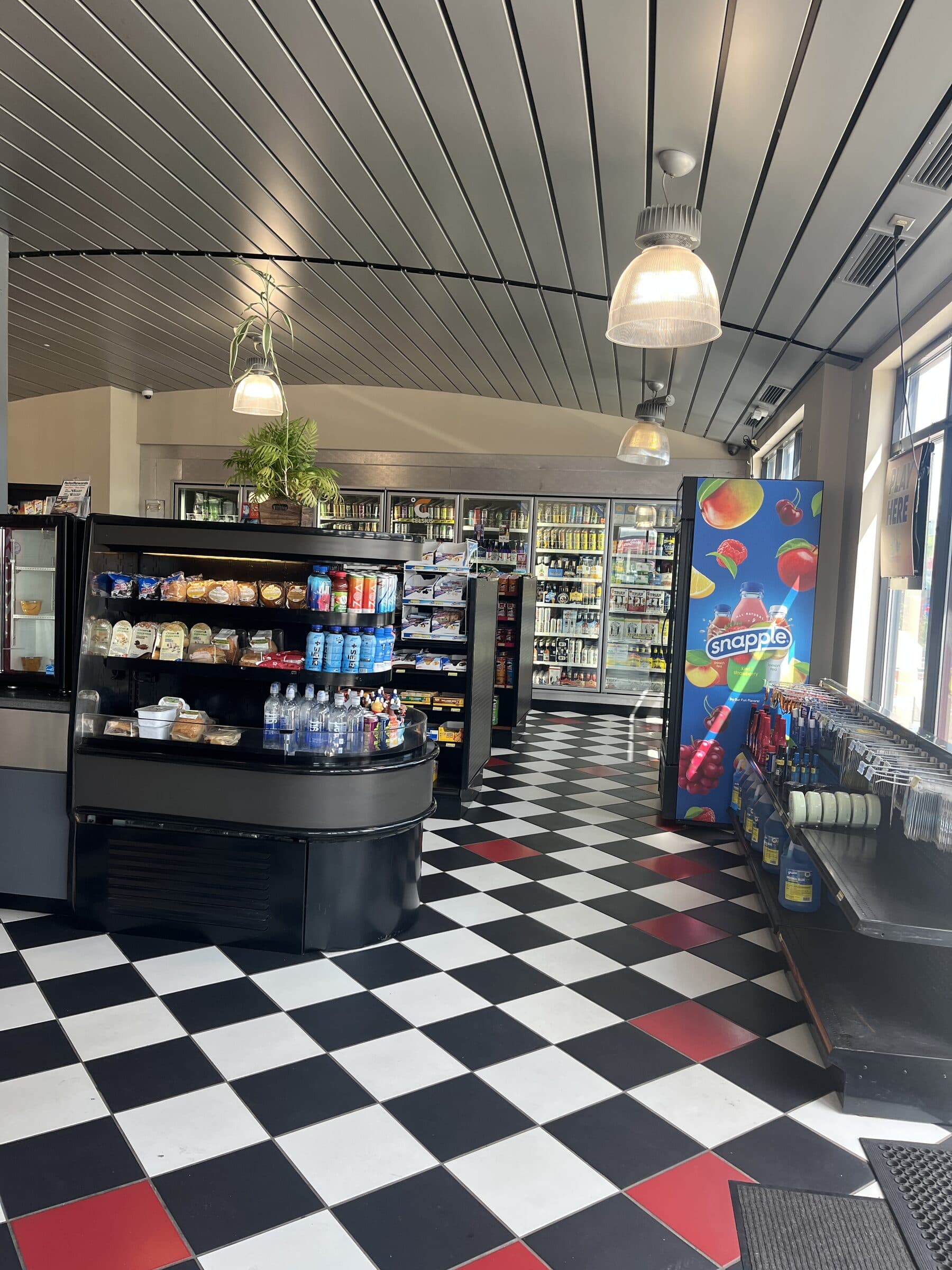 Bright convenience store interior with a black, white and red checkerboard floor, a grab-and-go case and a wall of drink coolers