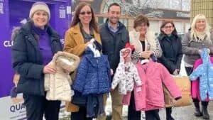 Group of women and a man holding donated children's winter coats outside a Cradles to Crayons display
