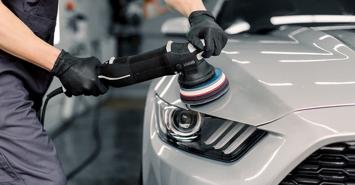 Gloved detailer polishing the hood of a silver car with a dual-action polisher
