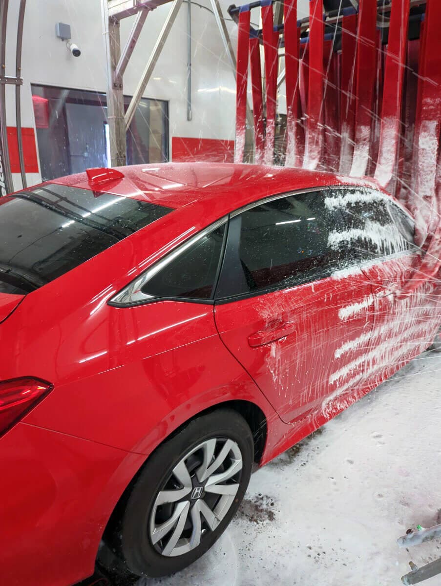 Red sedan getting sprayed as it passes under red cloth wash strips in the tunnel