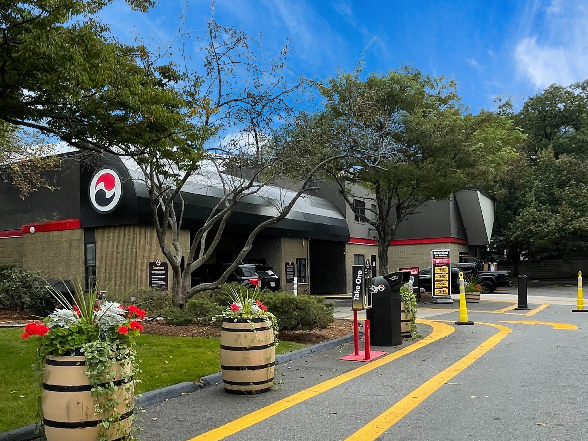 Whiskey-barrel planters with red geraniums along the entrance lane at ScrubaDub Natick