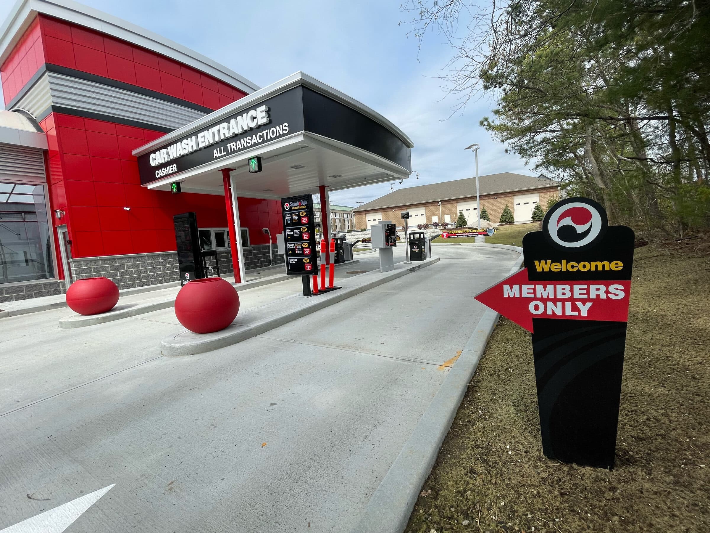 Welcome Members Only arrow sign beside the Car Wash Entrance canopy and red planters at ScrubaDub Coventry