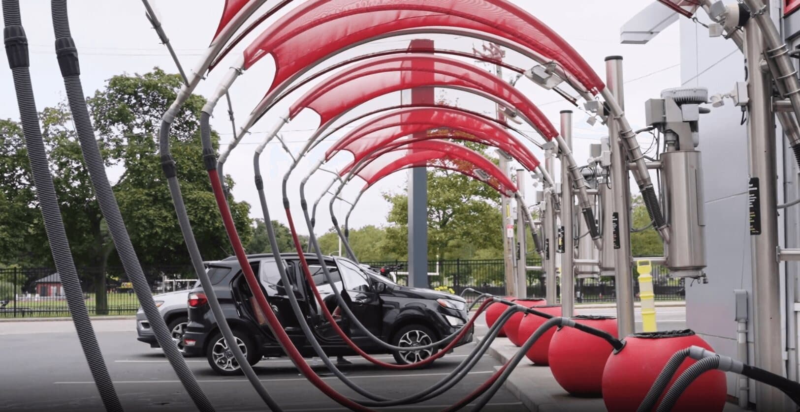 Rows of vacuum hoses under red mesh canopies with red ball trash cans and a car being cleaned