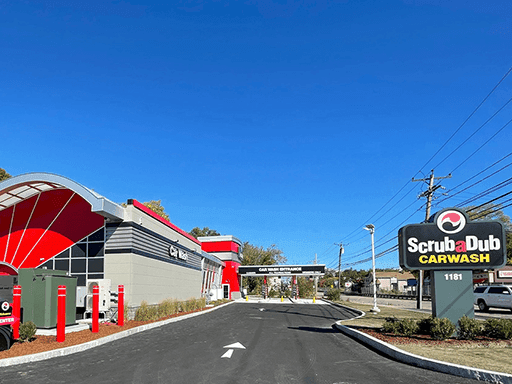 ScrubaDub Framingham car wash entrance drive with a ScrubaDub Carwash sign and red bollards