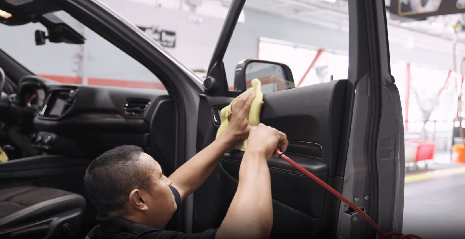 ScrubaDub attendant wiping the inside of an SUV door with a yellow microfiber towel and an air hose