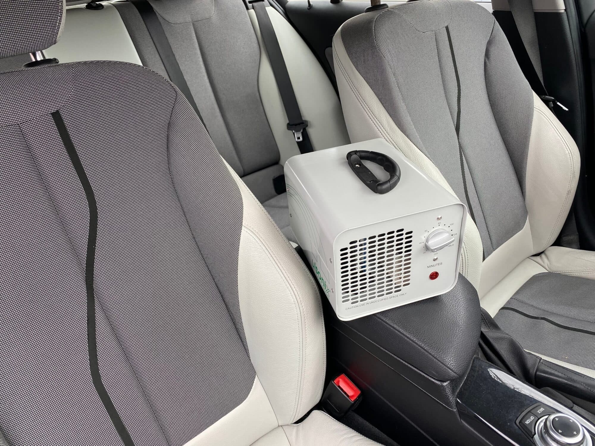 Portable ozone generator sitting on a car's center armrest between the front seats