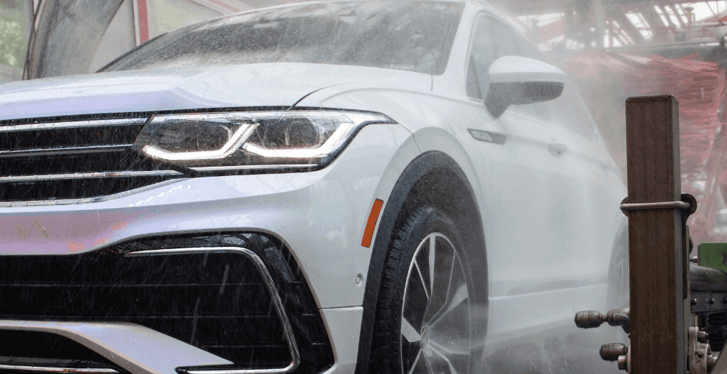 White SUV with headlights on being sprayed with water inside a car wash tunnel