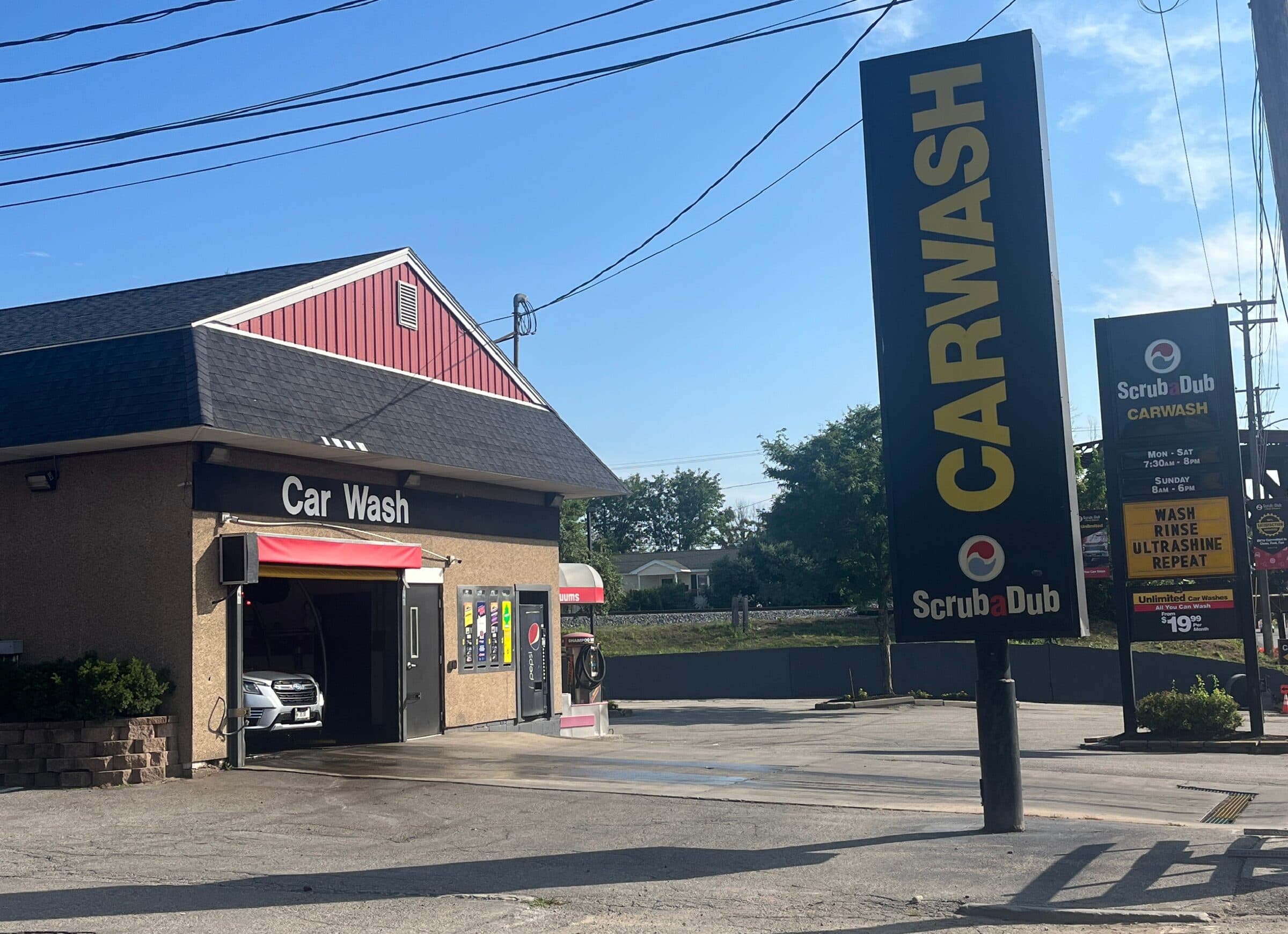 Small ScrubaDub car wash building with a red gable and an SUV in the wash bay beside tall CARWASH signs in Biddeford