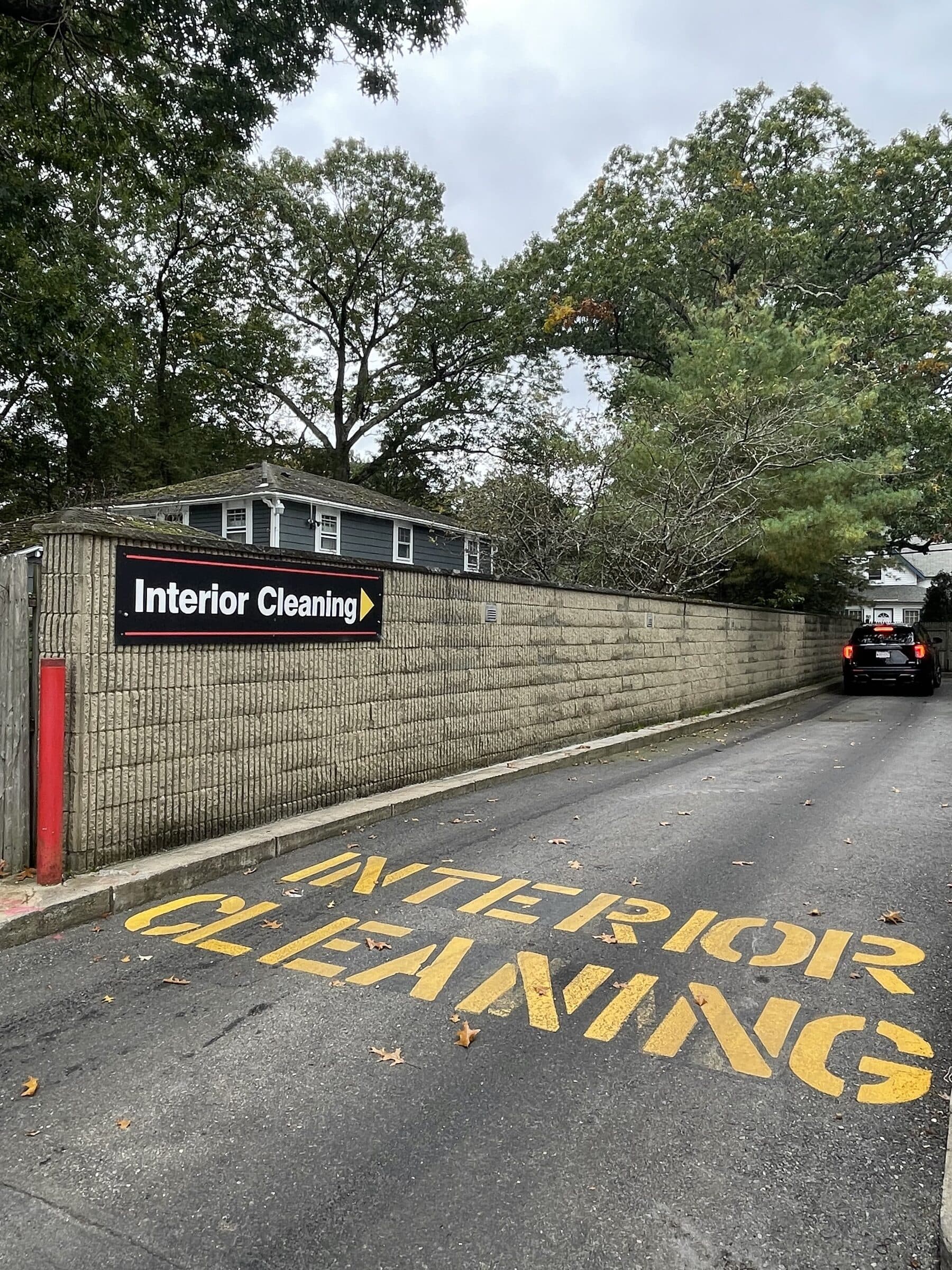 "Interior Cleaning" painted in yellow on a driveway beside a wall sign pointing the same way