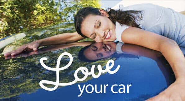 Smiling woman resting her head on the glossy hood of a blue car, her reflection visible in the paint