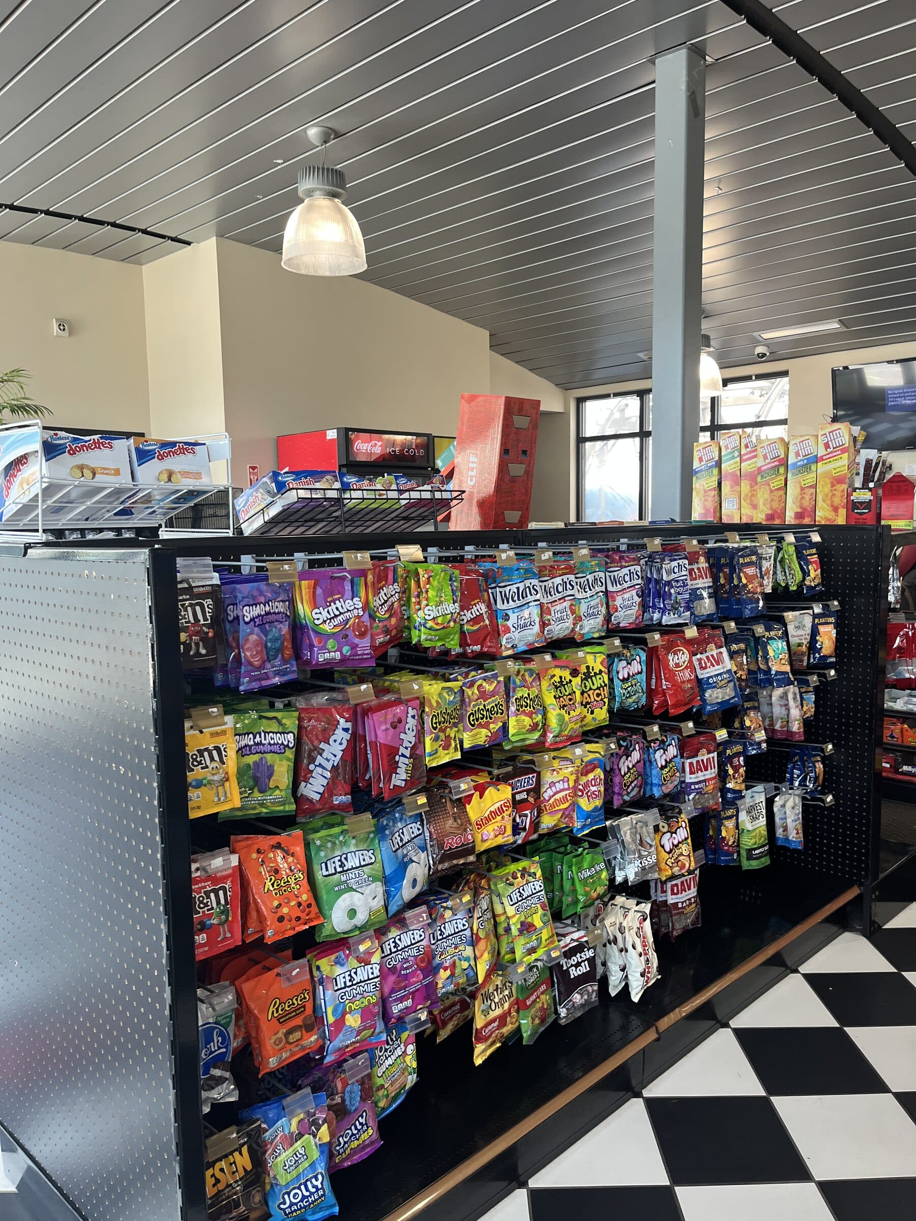 Convenience store candy rack packed with bags of Skittles, Twizzlers, Life Savers and other sweets above a checkered floor