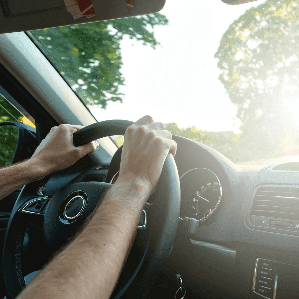 Driver's hands on a steering wheel with sunlight streaming through the windshield