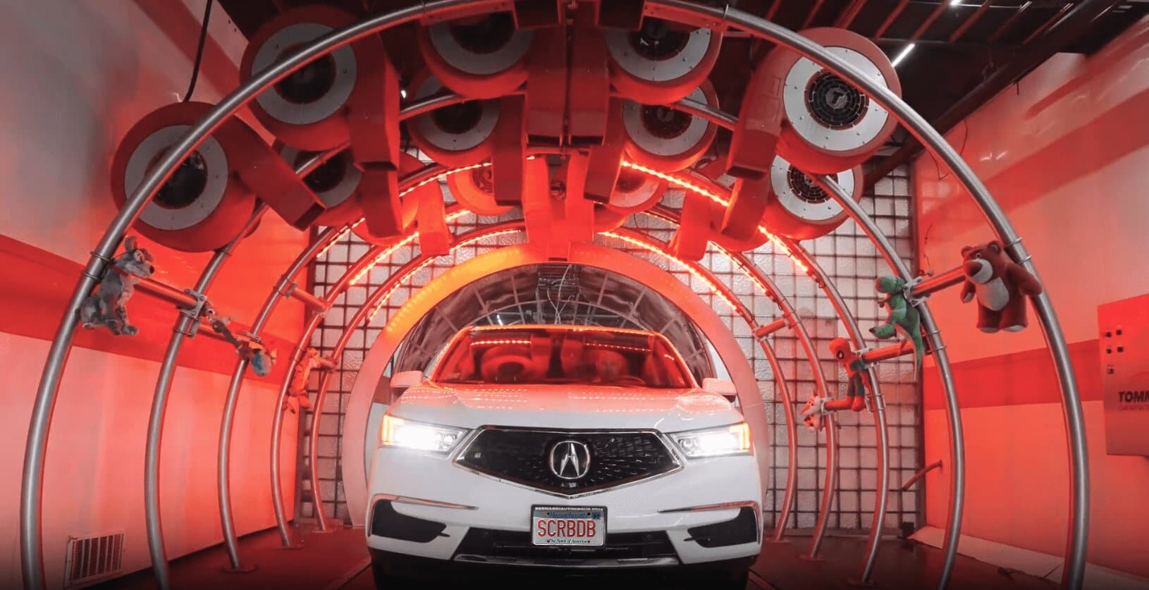 White SUV with a SCRBDB plate under red-lit dryer blowers decorated with plush toys