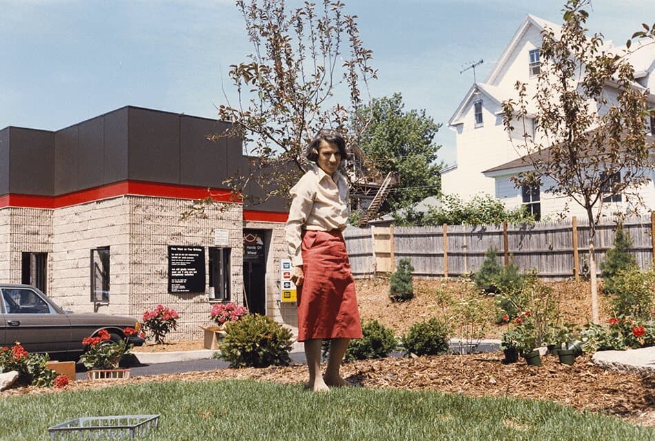 Elaine Paisner standing on a landscaped lawn in front of a ScrubaDub car wash building