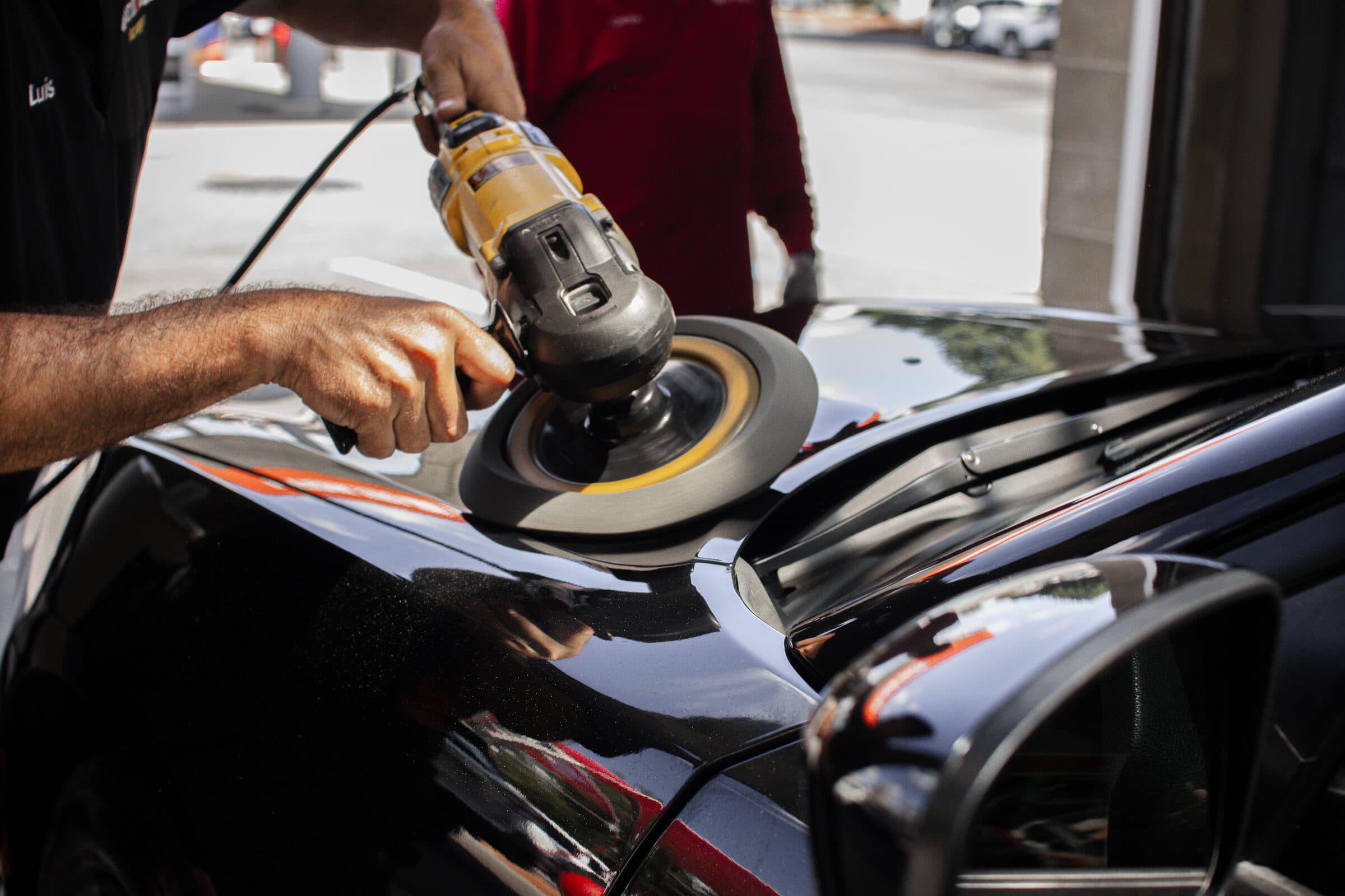 Close-up of a ScrubaDub detailer machine-polishing the glossy hood of a black car