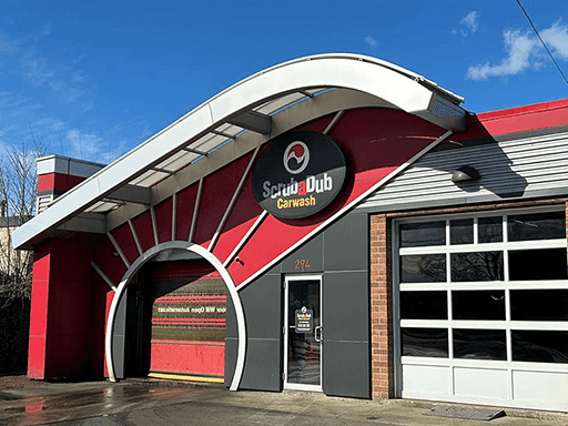 ScrubaDub Chelsea car wash with a red sunburst arch over the tunnel entrance and a curved white canopy