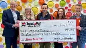 ScrubaDub team presenting a giant $39,765 check to Community Servings in front of a colorful pot-lid wall