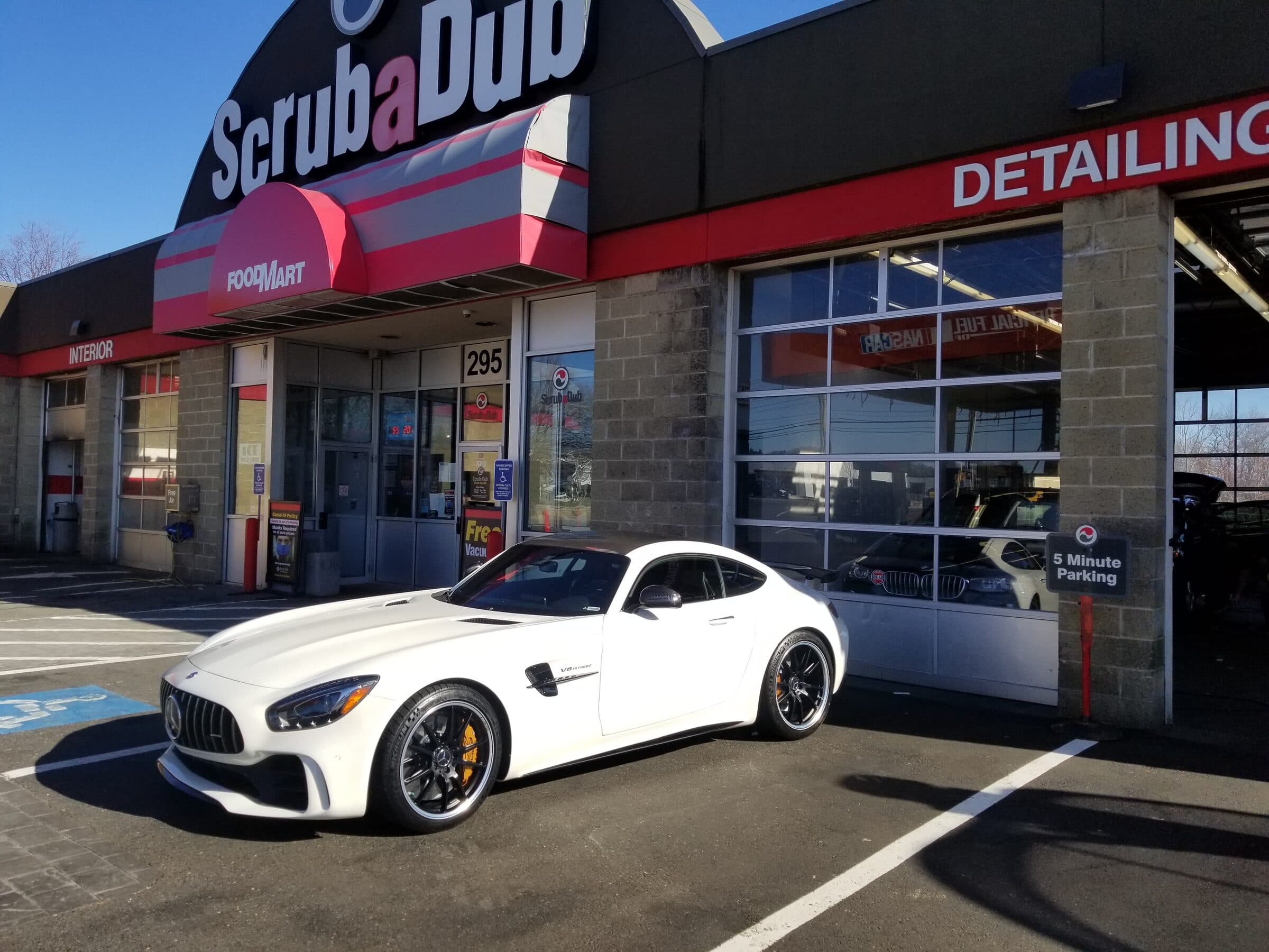 White Mercedes-AMG sports car parked outside a ScrubaDub Food Mart and detailing center