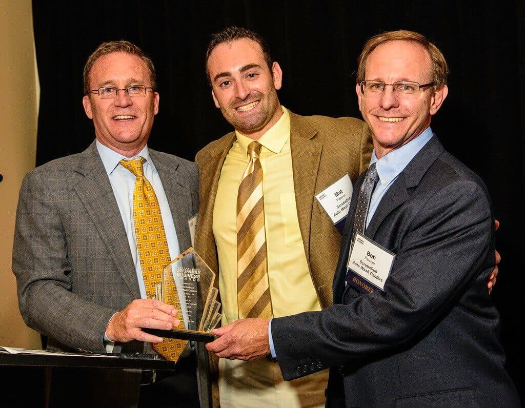 Mat Paisner and Bob Paisner of ScrubaDub smiling with a presenter while holding a 2013 Family Business Awards trophy