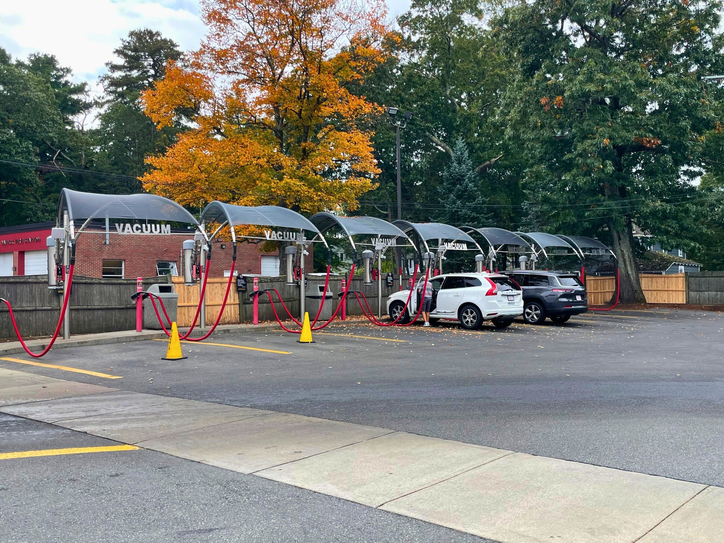Row of free vacuum stations with gray arched canopies and red hoses under orange fall foliage