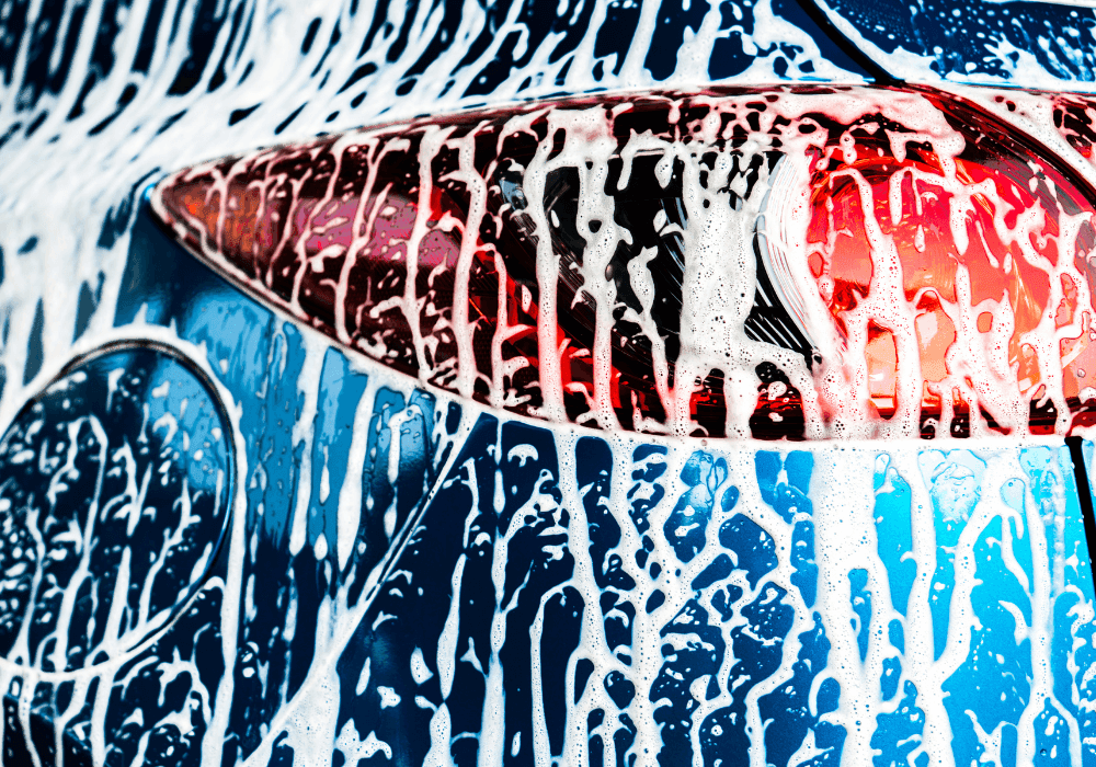Close-up of white soap suds streaming down a blue car's taillight