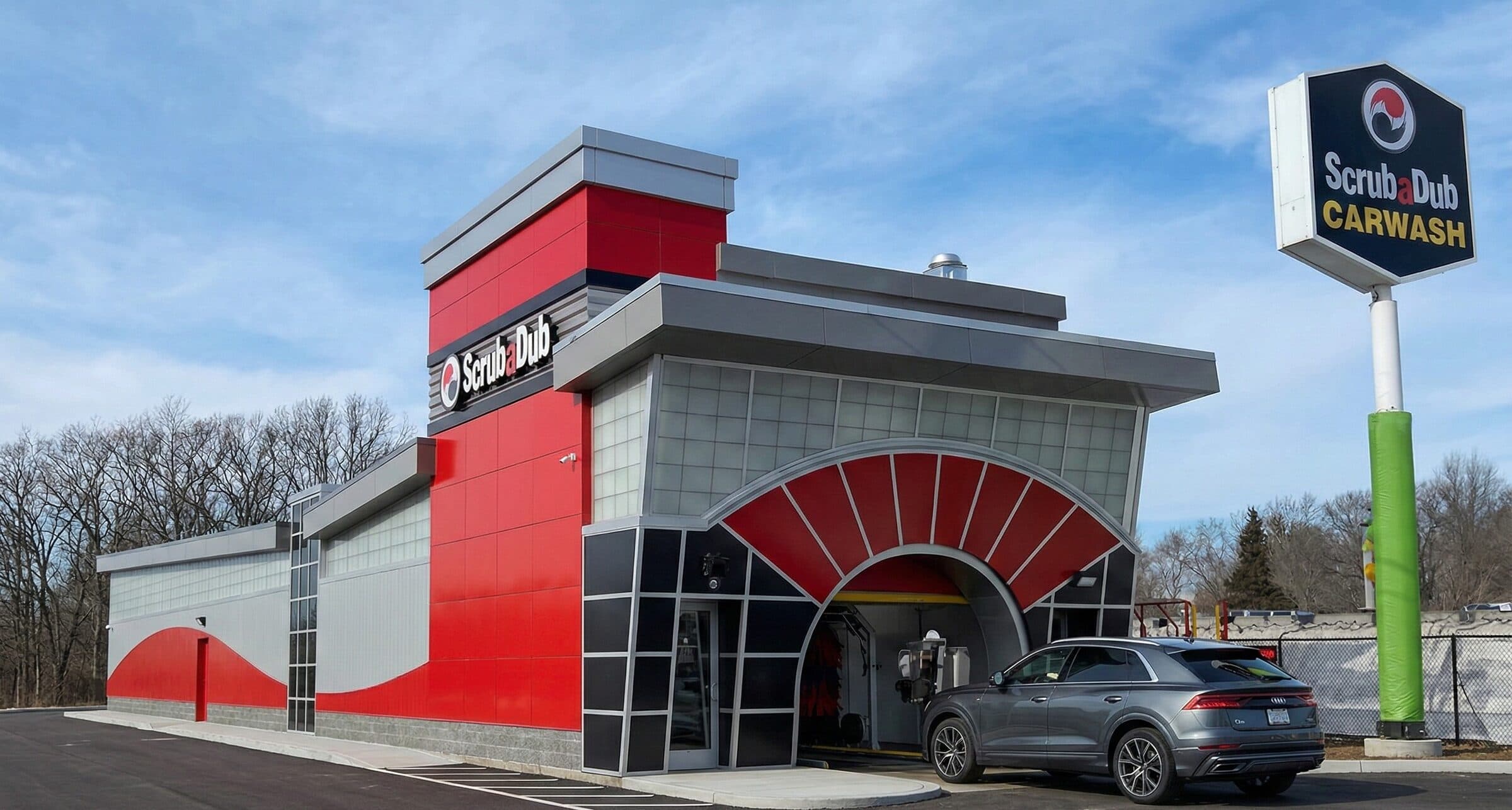 New red and gray ScrubaDub Medford car wash building with a sunburst arch, as a gray Audi SUV enters the tunnel