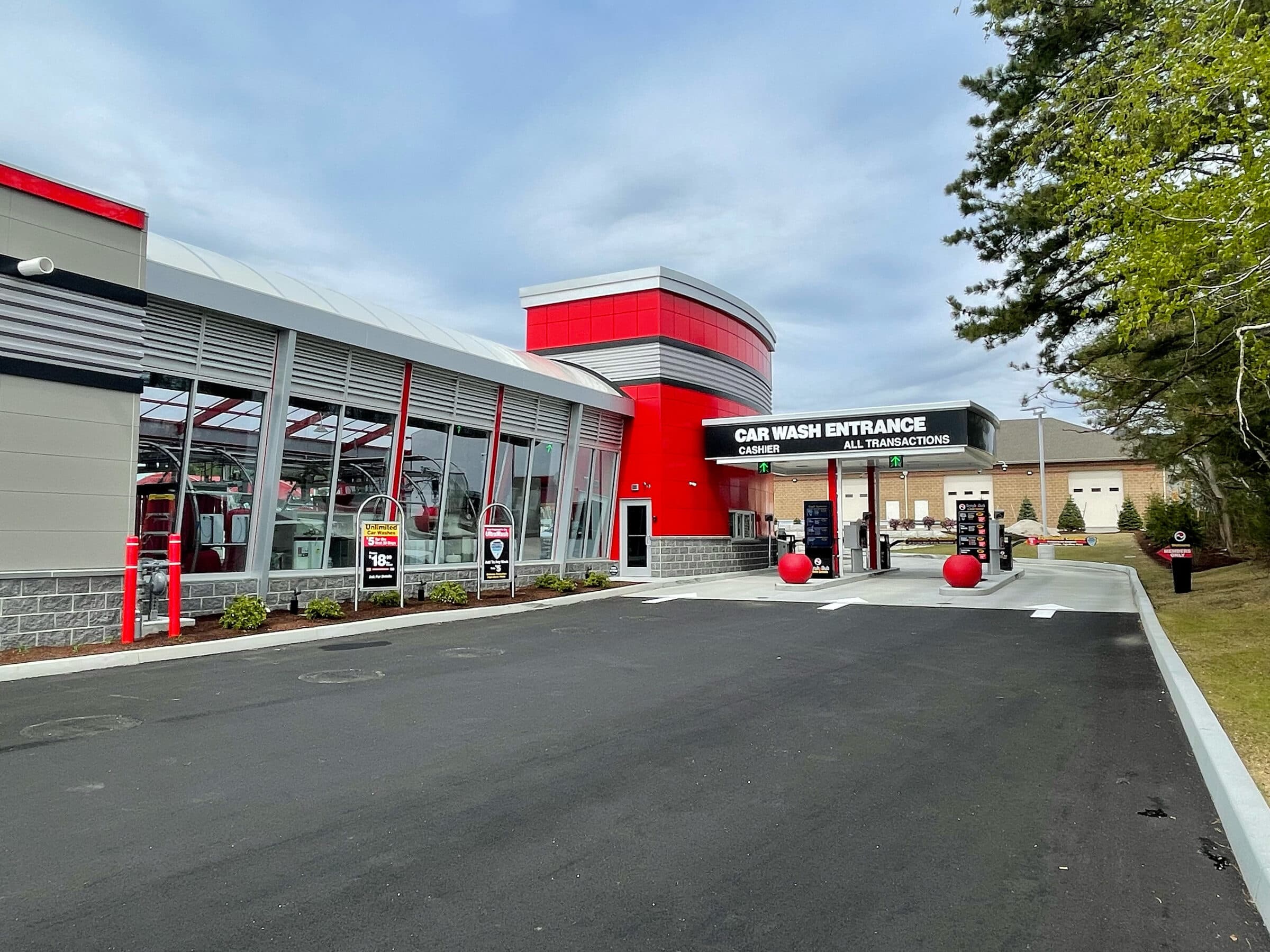 Modern ScrubaDub building with a glass-walled tunnel and a Car Wash Entrance canopy with red ball bollards