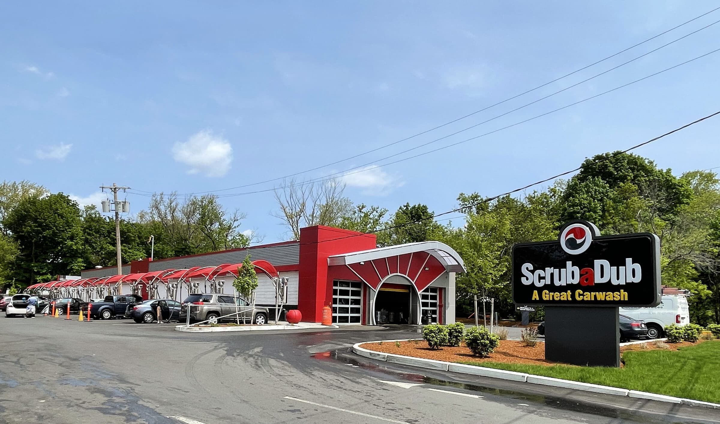 ScrubaDub Roslindale car wash with a red fan-arch entrance, a long row of red vacuum canopies, and a "ScrubaDub A Great Carwash" sign