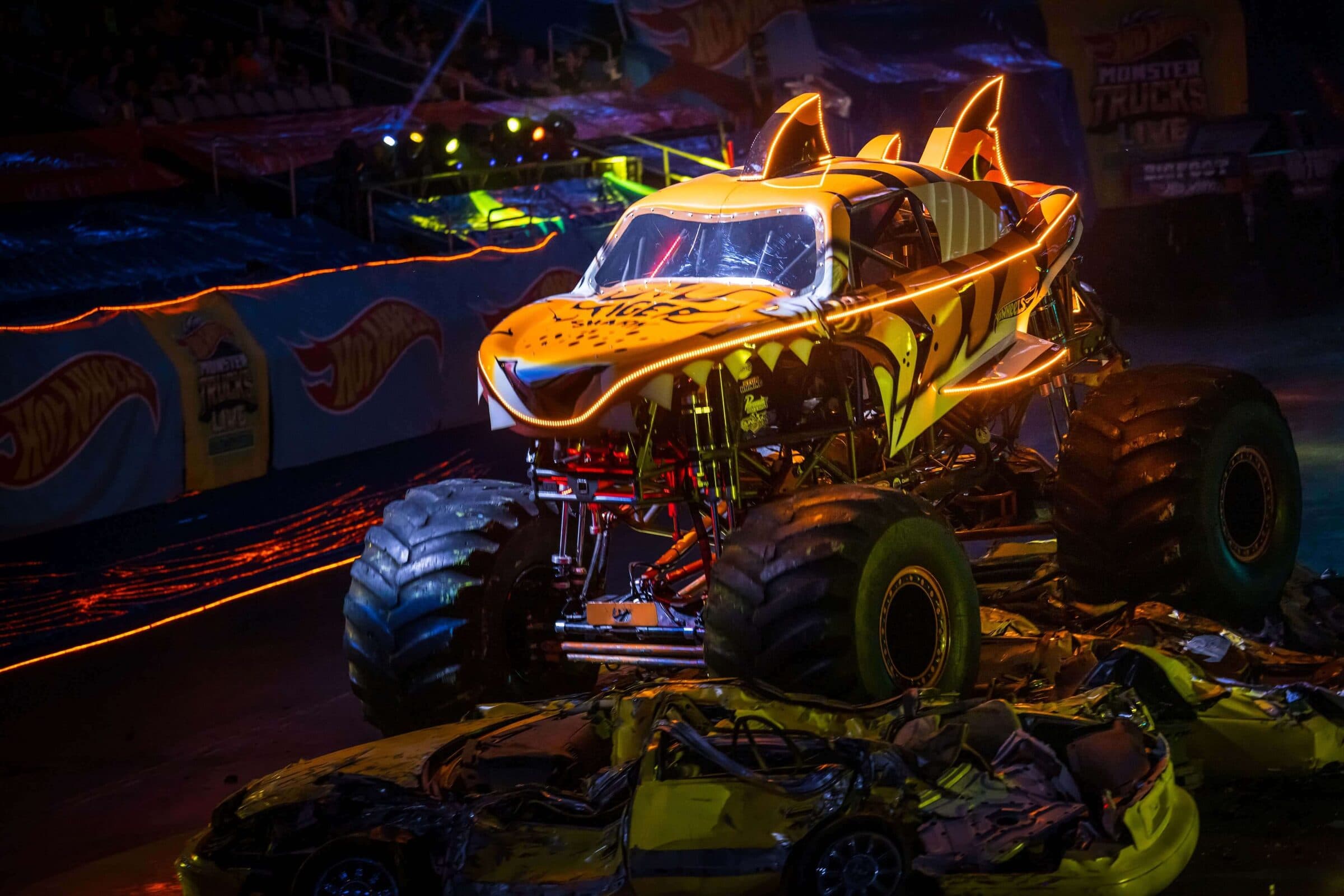 Tiger Shark monster truck with glowing orange lights crushing cars in a dark arena