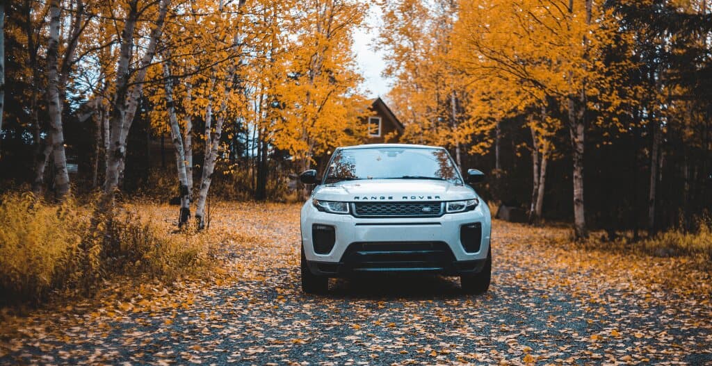 White Range Rover parked on a leaf-covered driveway under golden autumn trees