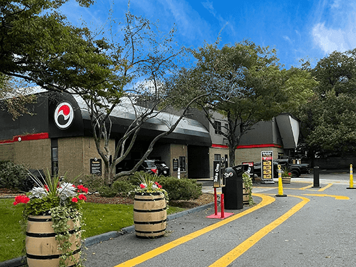ScrubaDub Natick entrance lane with yellow lane lines, flower barrels and a dark building among trees