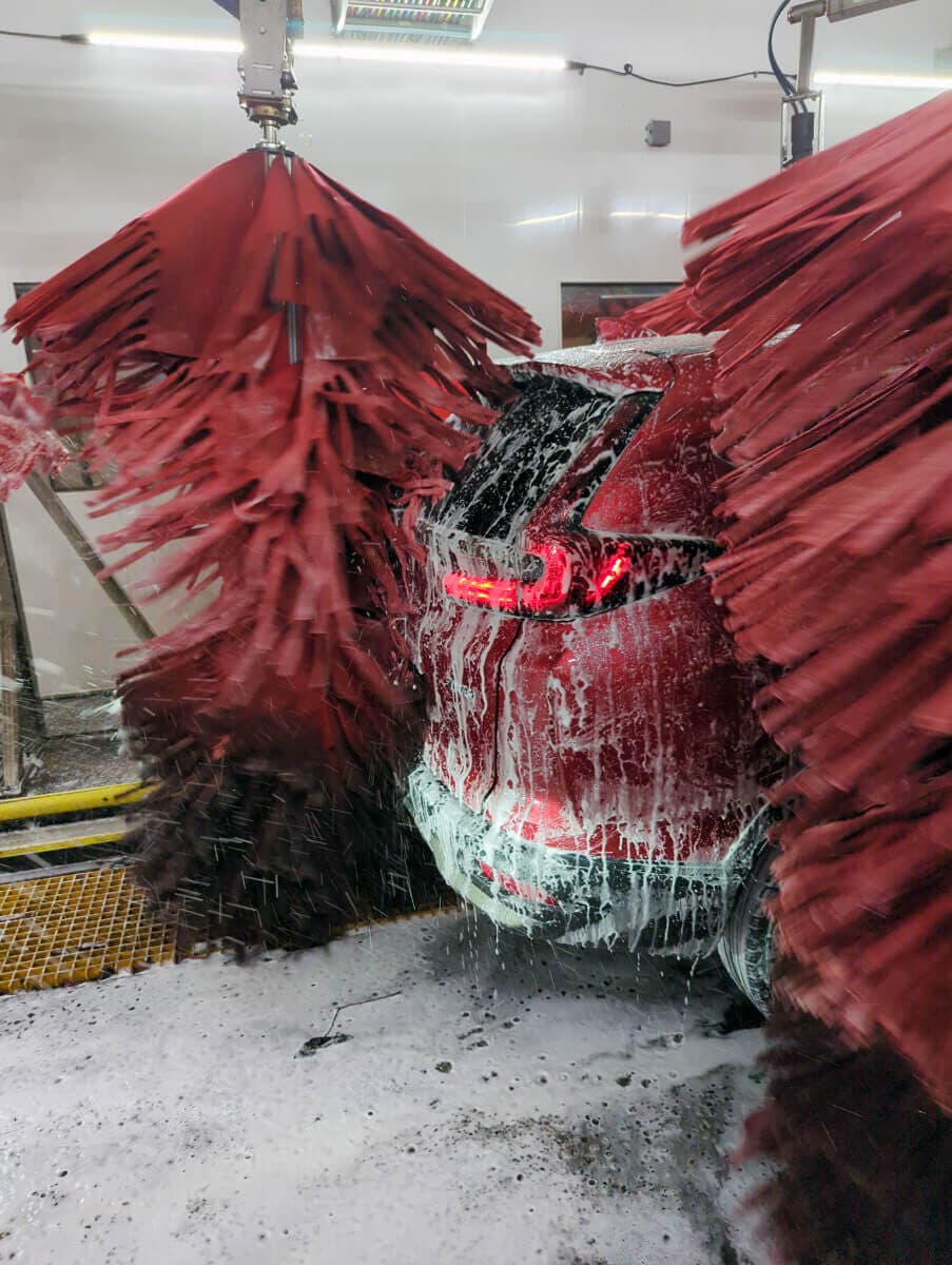 Foam-covered red SUV between spinning red wash brushes in the tunnel