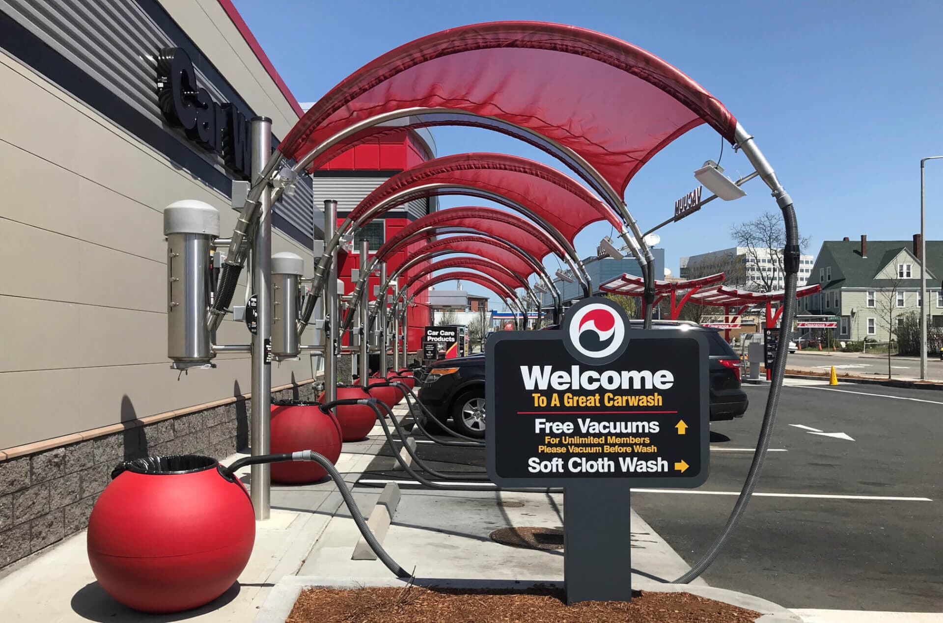 "Welcome to a great carwash" sign in front of a row of red vacuum canopies and red ball trash cans