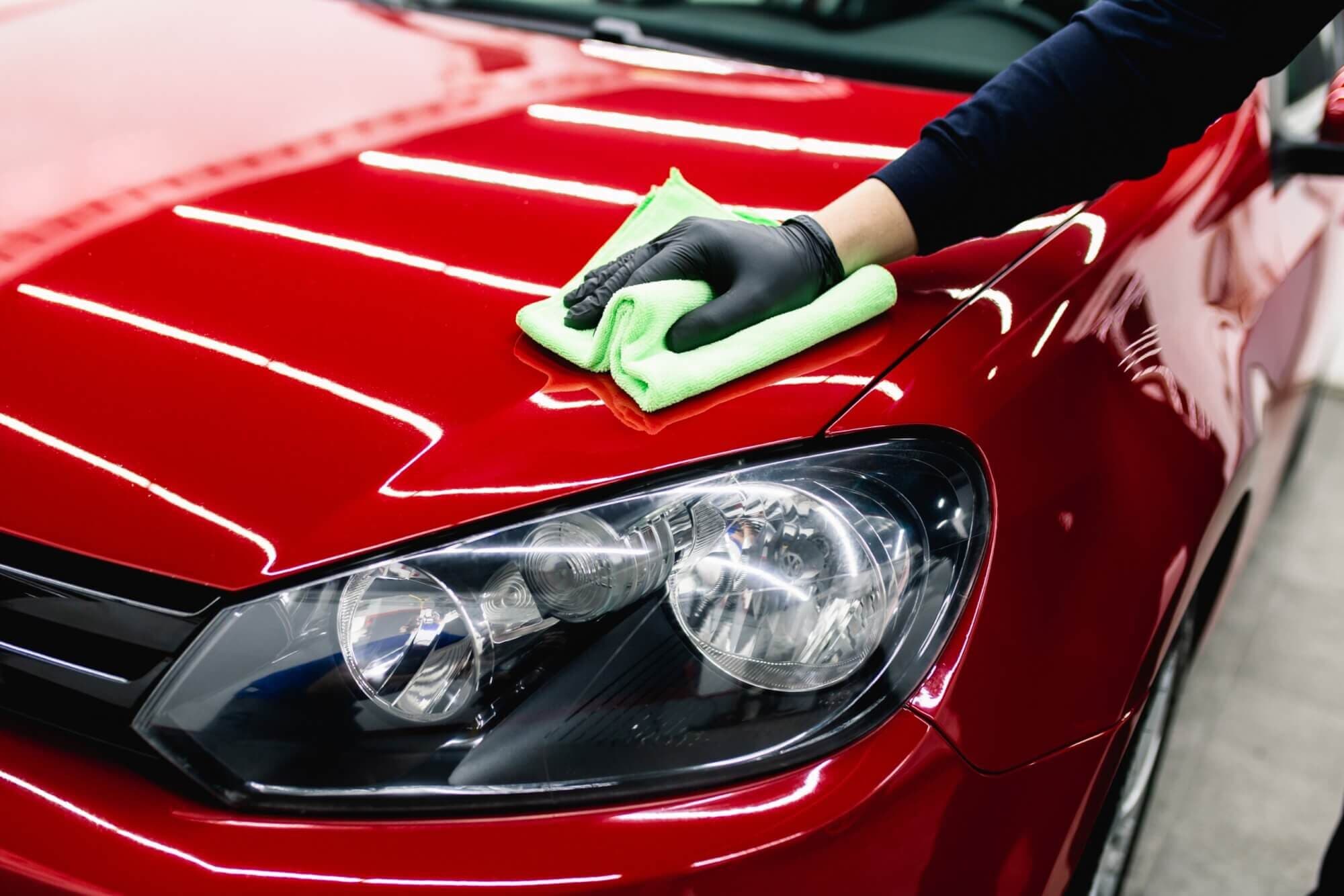 Gloved hand buffing the glossy hood of a red car with a green microfiber towel