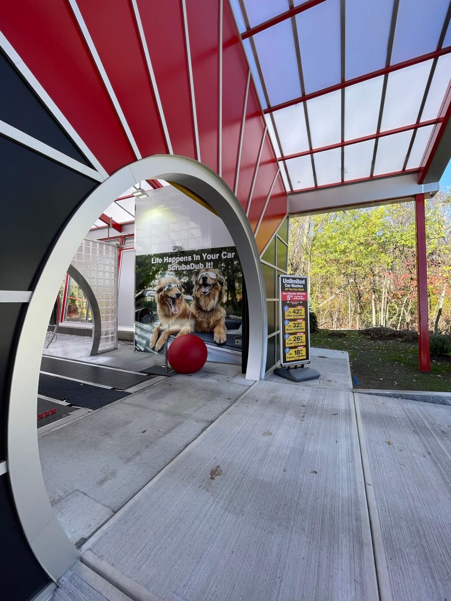 White arch framing a car wash tunnel entrance with a golden retriever mural and an Unlimited price sign