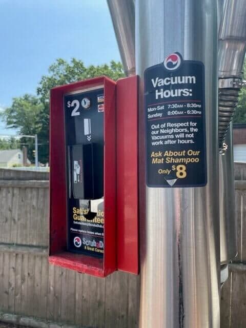 Red $2 payment box and a "Vacuum Hours" sign on a stainless vacuum pole