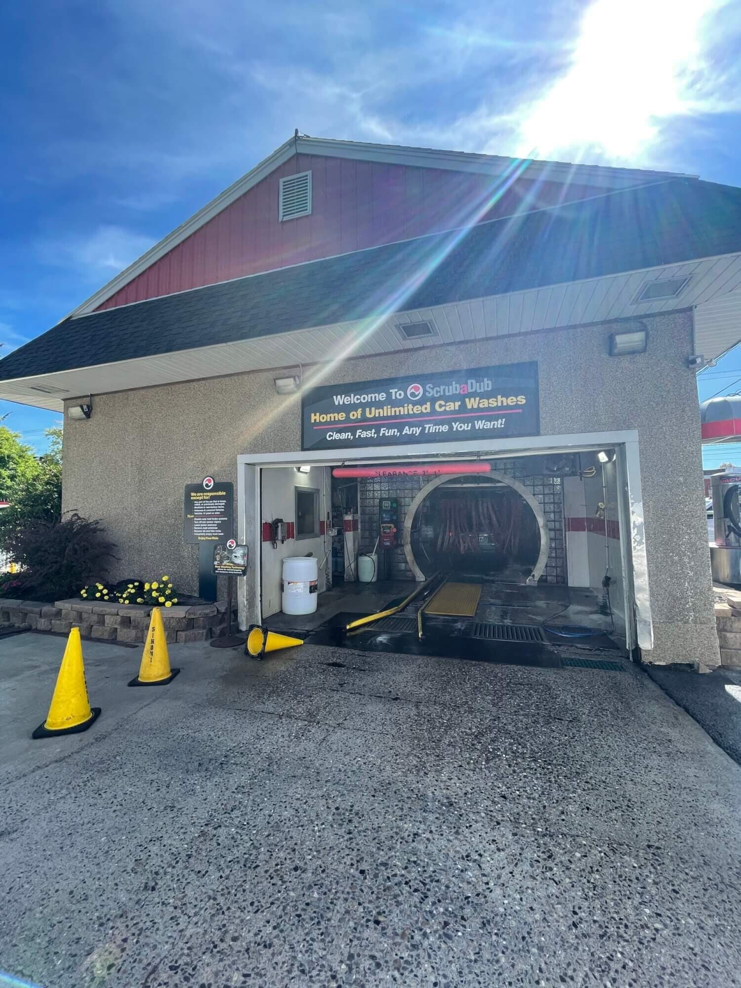 ScrubaDub Biddeford tunnel entrance with a "Home of Unlimited Car Washes" sign and strong sun flare