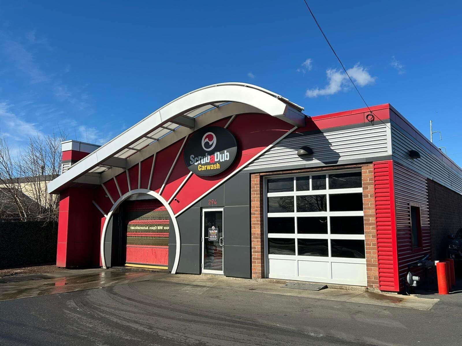 ScrubaDub Carwash building with a curved white canopy and red fan-shaped entrance arch under a blue sky