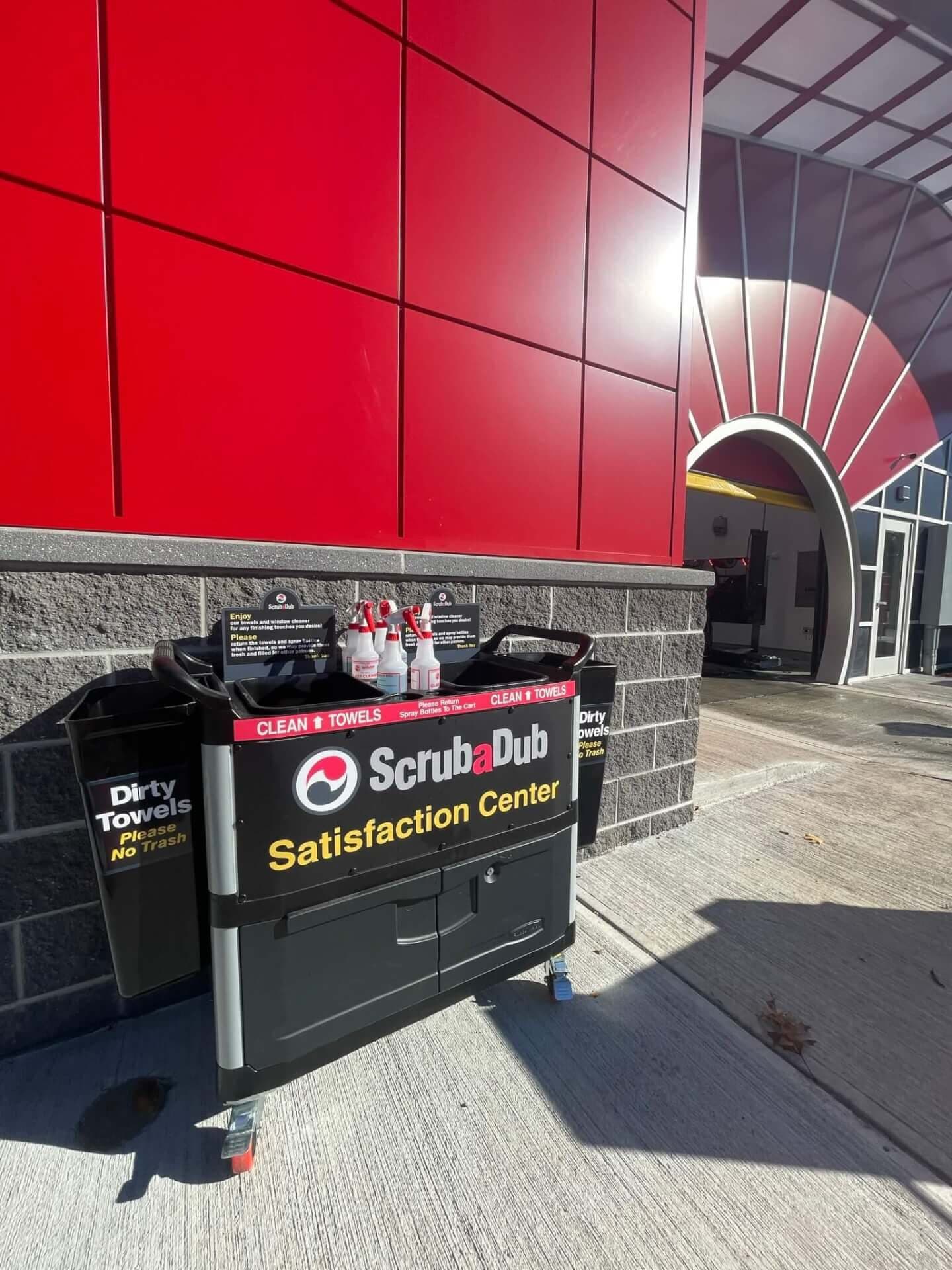 ScrubaDub Satisfaction Center cart with clean towels and spray bottles beside a red building