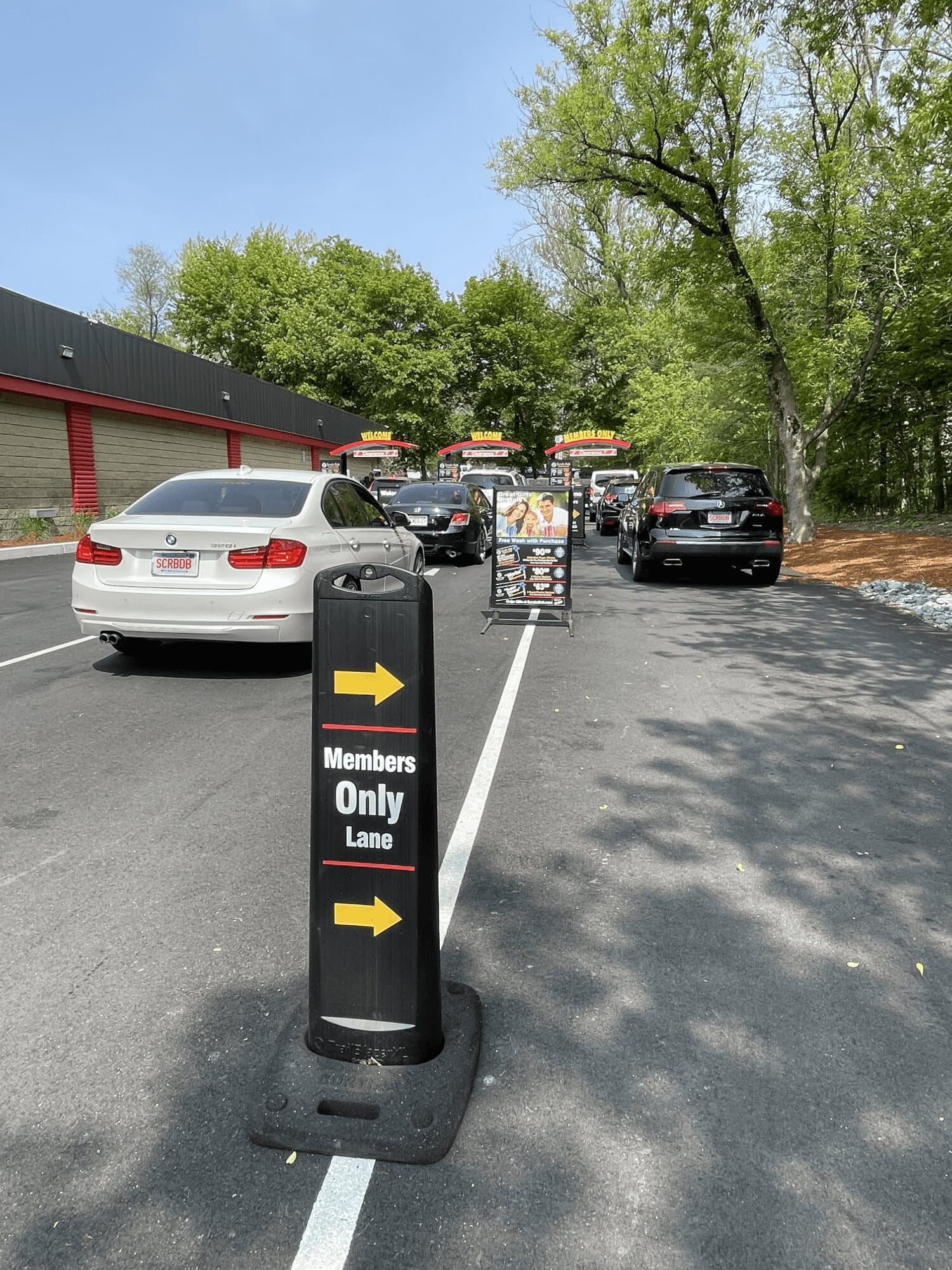 Members Only Lane sign in front of a line of cars waiting at the ScrubaDub Roslindale pay canopies
