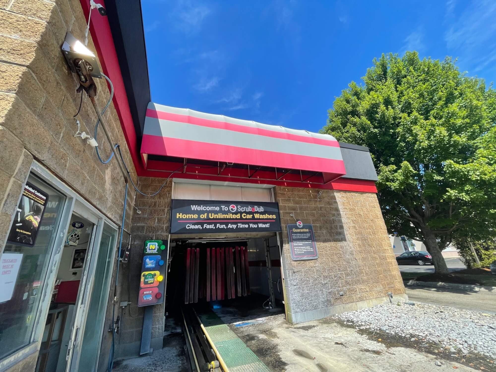 ScrubaDub Warwick tunnel entrance under a striped red-and-gray awning with a "Home of Unlimited Car Washes" sign