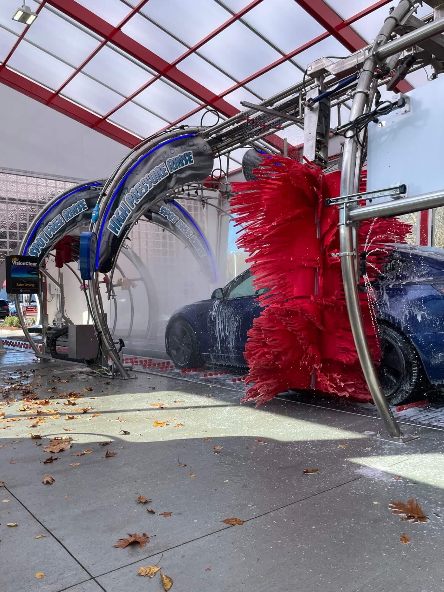 Soapy blue Tesla passing a red foam brush under "High Pressure Rinse" and "Spot Free Rinse" arches