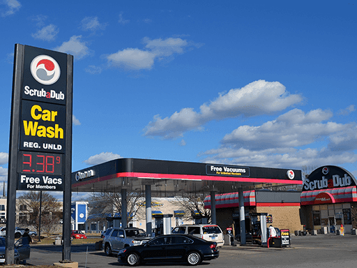 ScrubaDub Warwick pylon sign showing Car Wash, regular unleaded price and Free Vacs for Members, with the gas canopy behind
