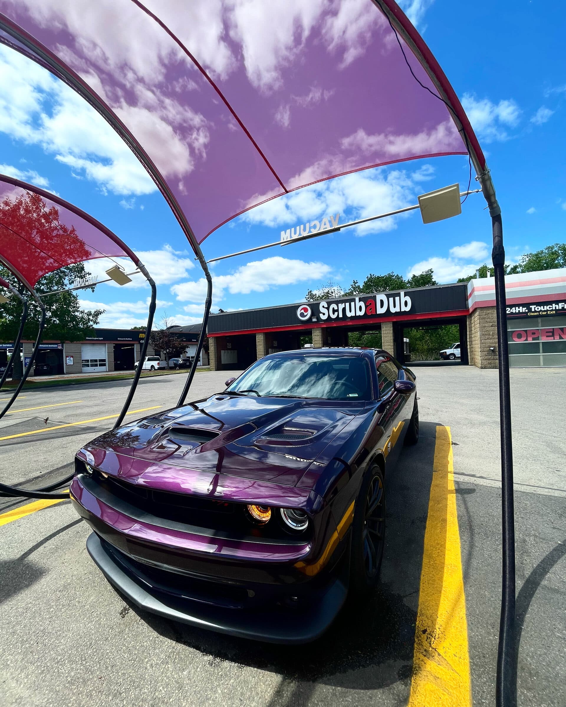 Purple Dodge Challenger parked under red vacuum canopies in front of the ScrubaDub Shrewsbury wash bays
