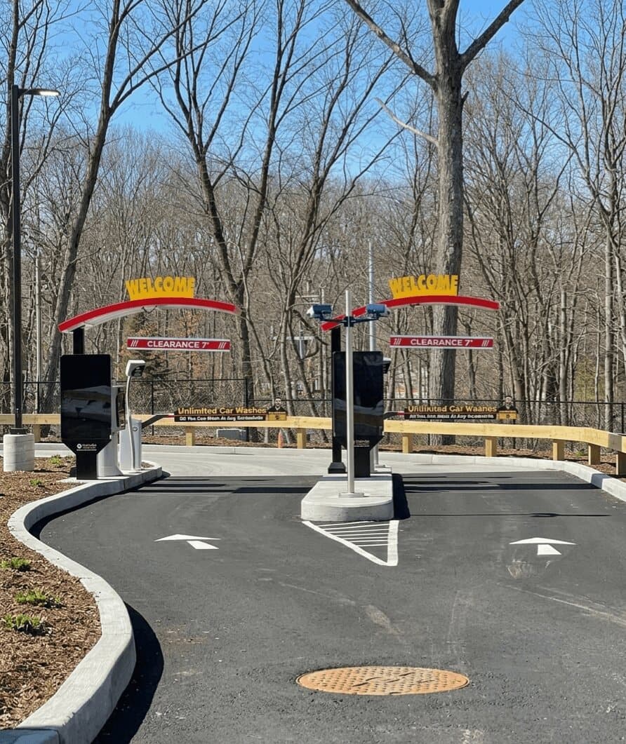 Two pay-station lanes at ScrubaDub East Greenwich under red and white WELCOME arches with clearance signs