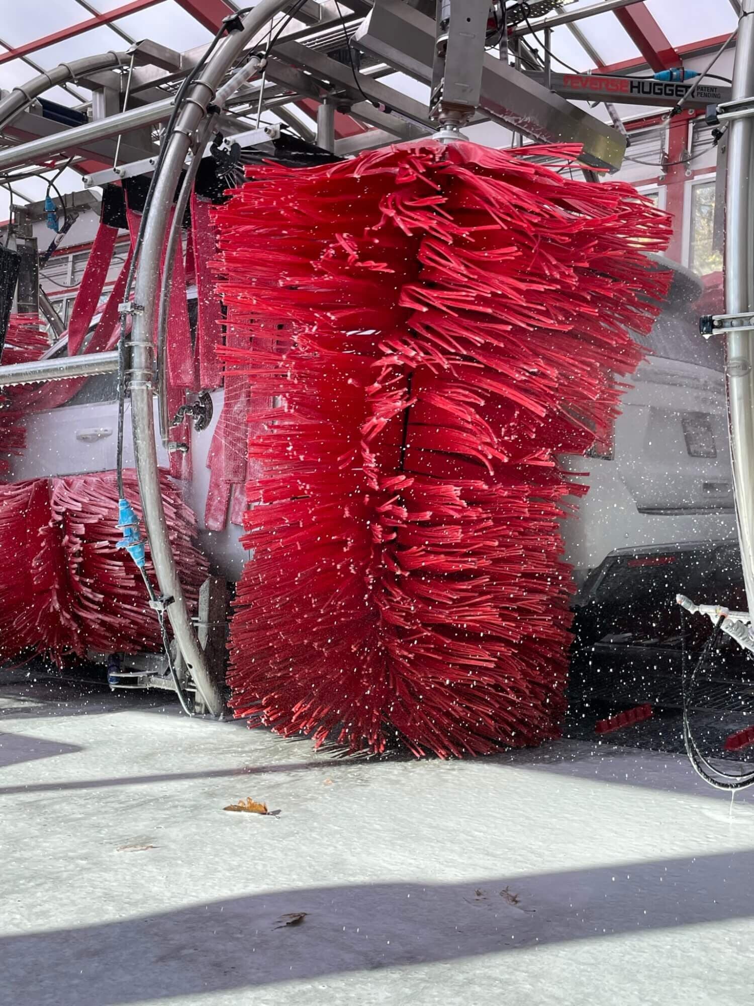 Close-up of a spinning red foam car wash brush scrubbing a white SUV